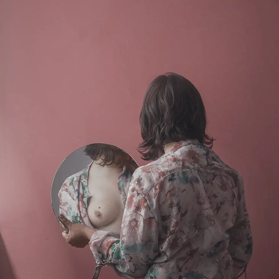 Portrait with a round mirror reflecting a fragment of the body.